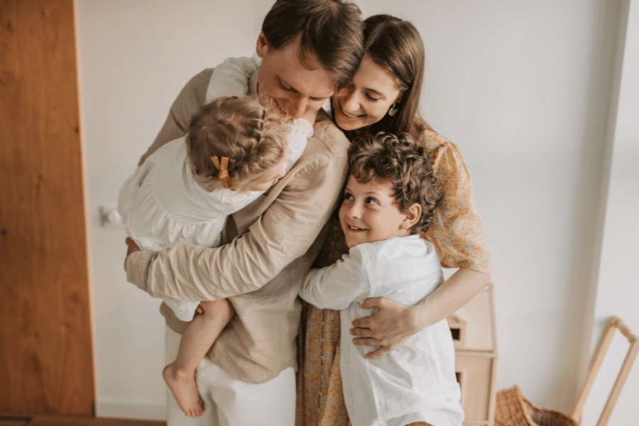 young family with two kids hugging and smiling at home 